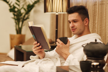 Handsome man having tea reading a book