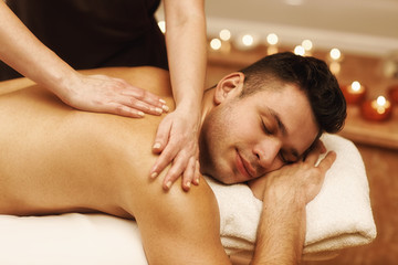 Obraz na płótnie Canvas Handsome young man enjoying massage at spa center