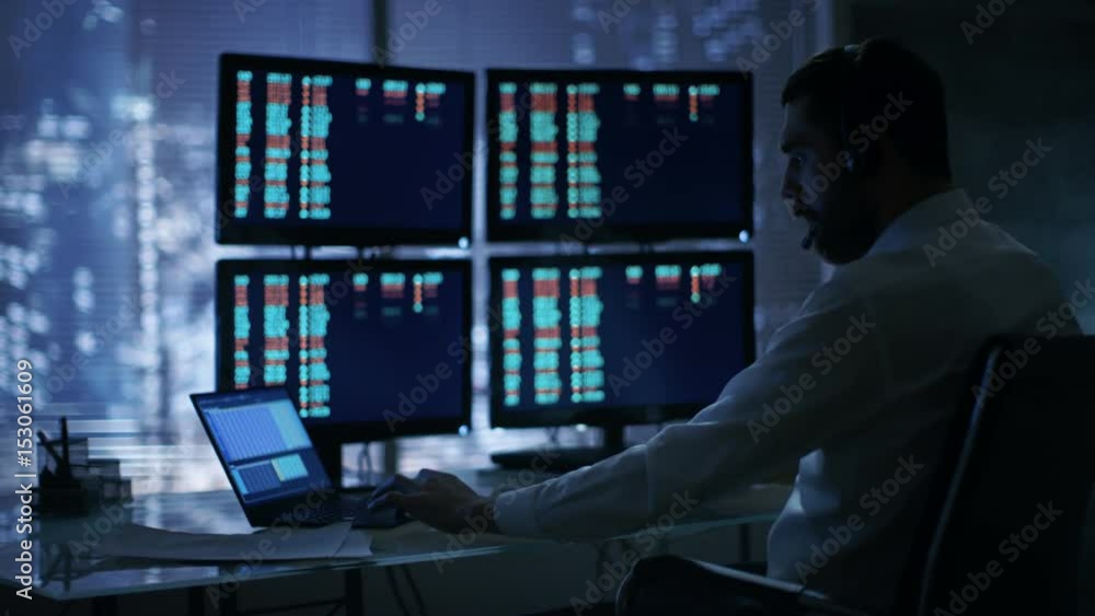 Poster Late at Night Trader Reads Numbers on His Multiple Displays with Stock Information on Them, He Also Consults Clients with Headset On. In Background Big City Window View. Shot on RED Cinema Camera 4K