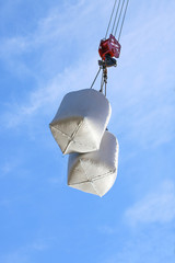 cargo in bags on hook of construction crane on sky background