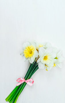 Bright yellow daffodils in vase on white wooden table with copy space. Yellow and white narcissus. Greeting card. Top view