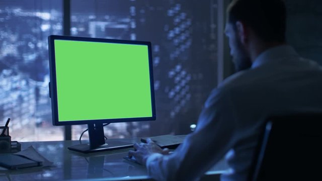 Late at Night Businessman Works on a Personal Computer with Green Mock-up Screen in His Private Office with Big City Window View. Shot on RED EPIC-W 8K Helium Cinema Camera.