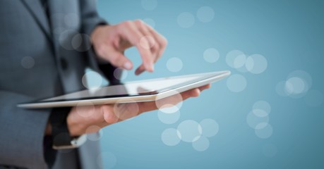 Business man mid section with tablet behind bokeh against blue background