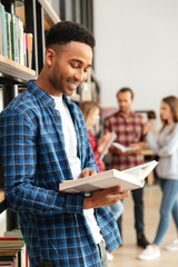 Student reading book while standing at the bookshelf