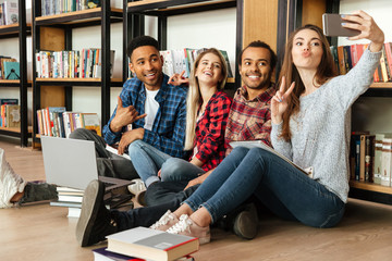 Happy students sitting in library make selfie by mobile phone.