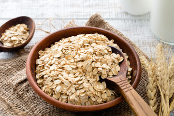 Rolled oats or oat flakes in bowl with wooden spoons, golden wheat ears and bottle of milk on background. Healthy lifestyle, healthy eating concept