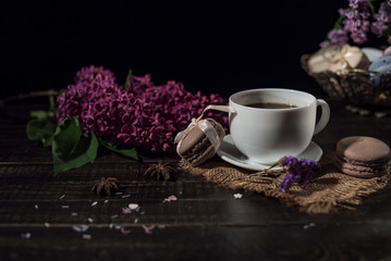 Coffee and cream macarons with cup of coffee and lilac on background