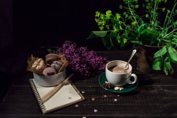 Obraz na płótnie Canvas Coffee and cream macaroons in a white plate with coffee cup, eco notebook with a pencil under lilac branch 