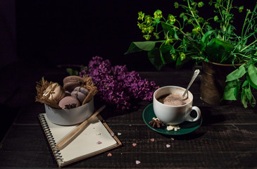 Obraz na płótnie Canvas Coffee and cream macaroons in a white plate with coffee cup, eco notebook with a pencil under lilac branch 