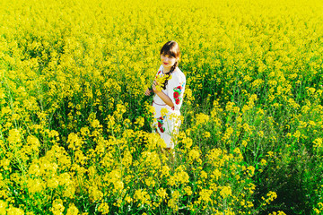 Fototapeta premium Beautiful young woman in Ukrainian embroidered standing in a field of yellow rape flowers