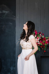 Obraz premium beautiful brunette girl in white wedding dress laughing with eyes closed,emotions with a smile is, sweeping the Studio, grey background, decoration with red flowers