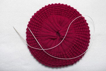 The process of knitting a red beret from a half-wool with circular knitting needles with a three-dimensional pattern
