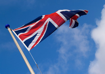 Union jack flag on flagpole, angled against blue sky.