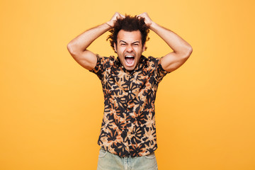 Screaming angry young african man standing over yellow background.