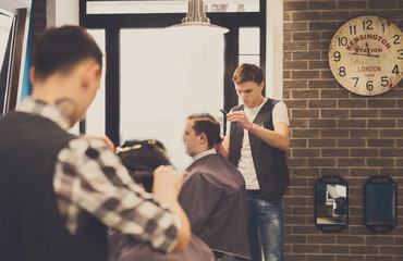 Fototapeta premium Man getting haircut by hairstylist at barbershop