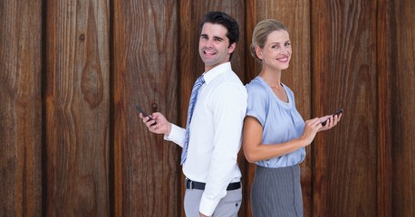 Smiling business people holding smart phone while standing back to back against wooden wall