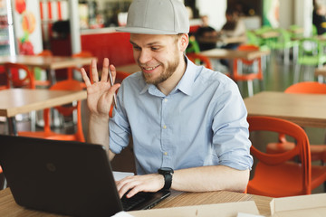 Portrait of a young man using laptop skype video chat at a cafe. Man with beard working on laptop...