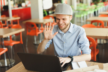 Portrait of a young man using laptop skype video chat at a cafe. Man with beard working on laptop...