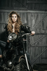 Fototapeta na wymiar Sexy pretty biker in leather jacket sitting on vintage motorcycle