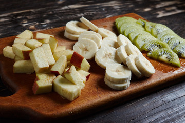 Sliced fresh fruit on a wooden board. Kiwi, banana, apple slices on the board.