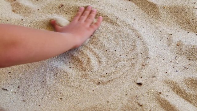 Closeup of little white child hand drawing heart shape with his fingers in sandy beach background. Real time full hd video footage.