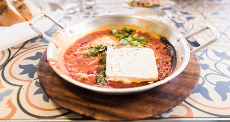 Shakshuka in a pan with cheese and bread - street food. Middle eastern traditional dishes. Fried eggs with vegetables and goat cheese . Middle eastern style breakfast or lunch.