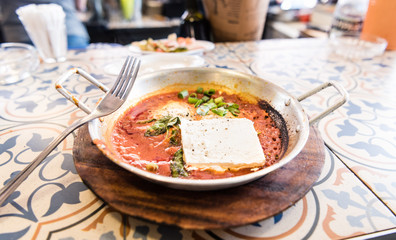 Shakshuka in a pan - street food. Middle eastern traditional dishes. Fried eggs with vegetables and goat cheese. Middle eastern style breakfast or lunch.