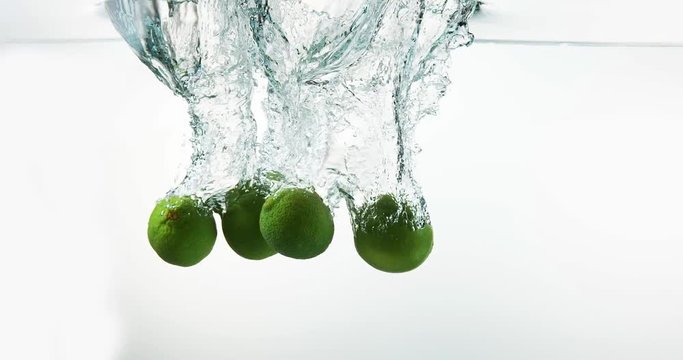 Green Lemons, citrus aurantifolia,, Fruits falling into Water against White Background, Slow Motion 4K