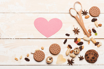 Wooden spoons, nuts, biscuits and pink heart on vintage background