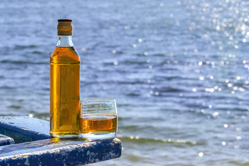Bottle and tumbler of whiskey on background of lake