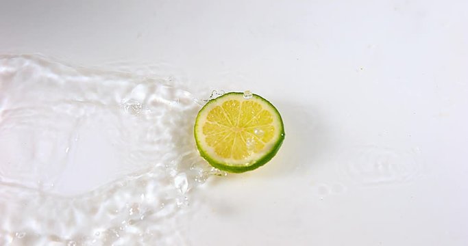 Green Lemons, citrus aurantifolia , Fruits falling on Water against White Background, Slow Motion 4K