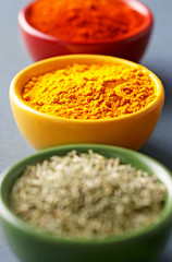 Spices in colorful bowls viewed from above. Various seasonings on a dark background. Chili pepper, curry powder, oregano. Red, yellow, green colors