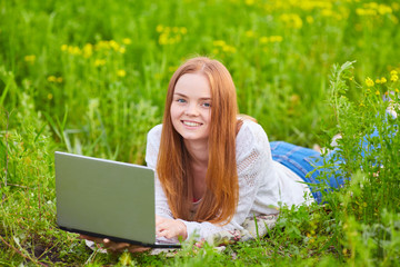 Smiling girl with laptop on grass