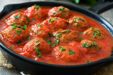 Meatballs with tomato sauce in iron frying pan on wooden table