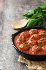 Meatballs with tomato sauce in iron frying pan on wooden table