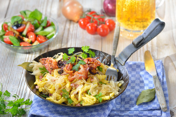 Deftige schwäbische Krautspätzle mit Speck und Röstzwiebeln rustikal  mit hellem Bier serviert - Swabian spaetzle with sauerkraut, fried bacon and onion rings on a wooden table with a Munich beer