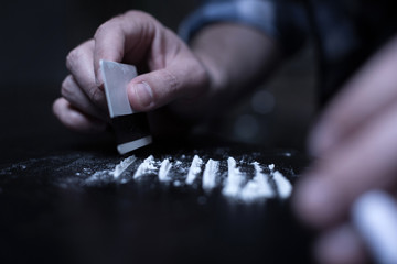 Skillful dope addict preparing cocaine lines in the dark place