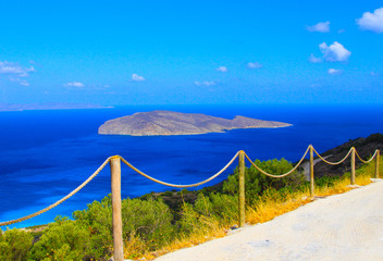 Fototapeta premium Island and road. A deserted island in the blue sea can be seen from the coastal road, enclosed by a fence of sturdy rope.