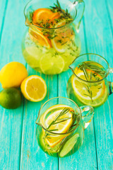 On the turquoise wooden surface there are decanters with detox lemonade, lemon, orange, lime,...
