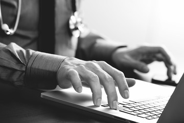 close up of smart medical doctor working with laptop computer and mobile phone and stethoscope on dark wooden desk