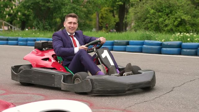 Young businessman in a suit driving Go-Kart car in a playground racing track.