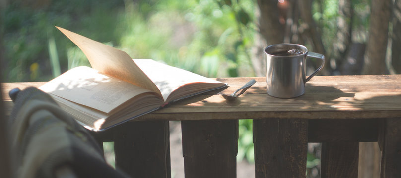 Metal mug, book and chair on a wooden terrace