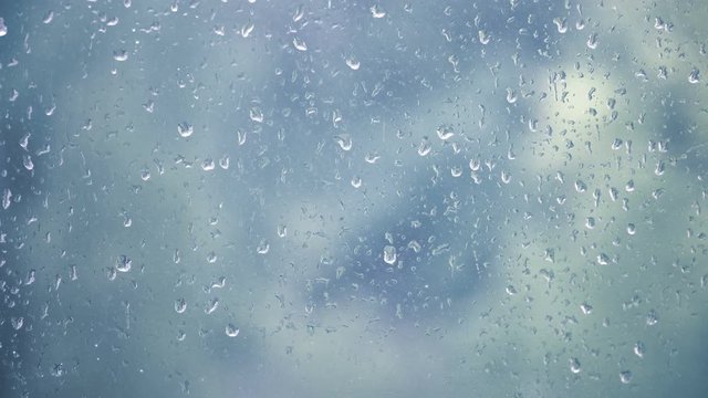 Rain drops on a window glass, background in shades of blue