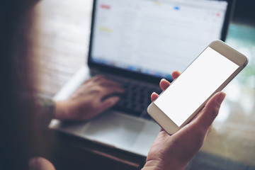 Mockup image of business woman holding mobile phone with blank white screen with latop on wooden table in cafe
