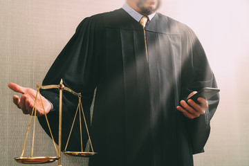 justice and law concept.Male judge in a courtroom with the balance scale and using smart phone