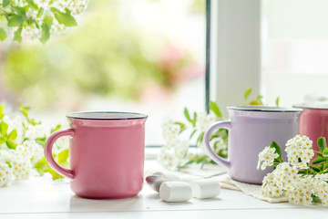 Hot cocoa with marshmallows in pink cups and fresh spring white flowers on the windowsill. Cozy home concept. Shallow depth of field.