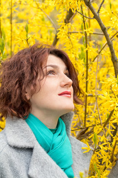 Pretty young red head woman with forsythia blossoms in spring park. Yellow blossoms background.