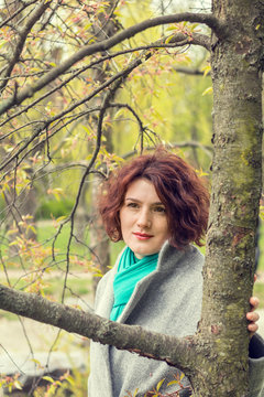 Pretty young red head woman close to the tree in spring park. Spring trees background.