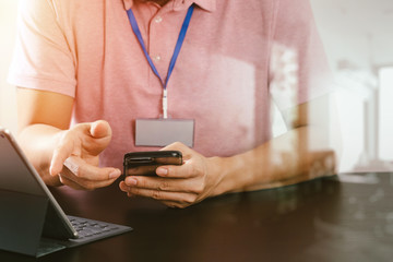 businessman in pink t-shirt working with smart phone and digitl tablet computer on wooden desk in modern office with glass reflected view