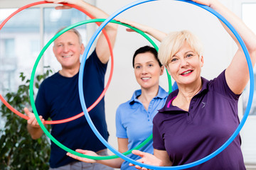 Senior couple in physiotherapy doing exercise with hula hoop © Kzenon